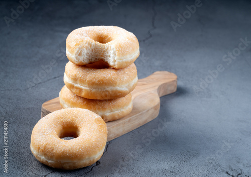 Perspective view of sugar donuts stacked on a wooden cutting board with one donut in the foreground on a gray background
