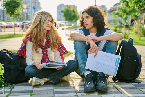 Two teenage students talking outdoors while studying together in city park