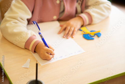 Child writing with blue pen at desk
