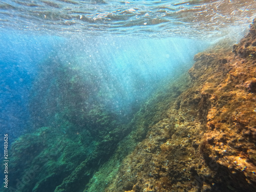 Fotografie Underwater view of rocky sea bottom with sun rays penetrating crystal clear turq