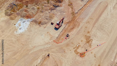 Aerial view showing a heavy excavator and various materials on a large, undeveloped construction site, preparing the ground for future urban development and infrastructure