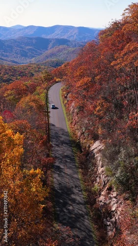 Car cruising on scenic road in mountains. Trees glowing in vibrant autumn foliage.