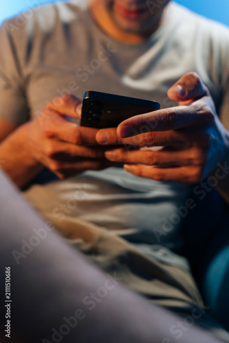 Close-up of man hands holding smartphone. Person scrolling or gaming at night. Modern lifestyle concept with cinematic blue and orange light. Shallow depth of field on mobile device.