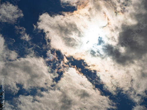 Sun shining through iridescent clouds in blue sky
