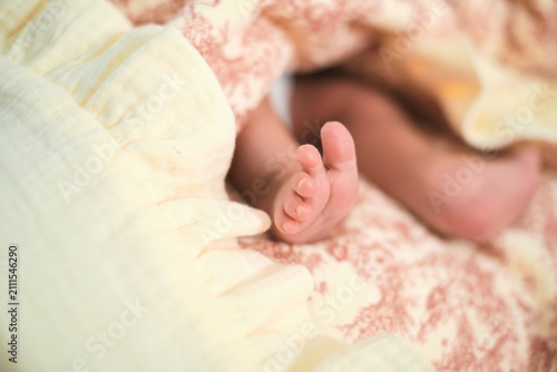 A newborn baby rests under soft pastel blankets, with tiny toes in sharp focus against a blurred face. The image reflects infant care, fragile life, family tenderness, and early parenthood.