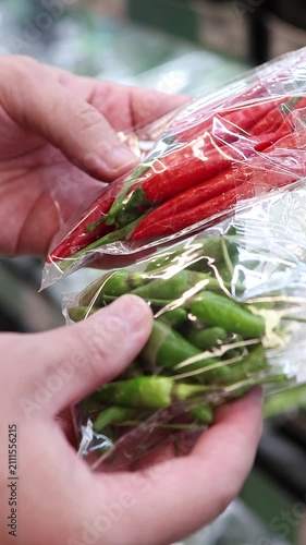 Customer Holding Fresh Red and Green Chili Peppers in Plastic Bags While Choosing Hot Ingredients at Grocery Store Produce Section. Close Up of Hands Buying Spicy Food. Vertical Footage.