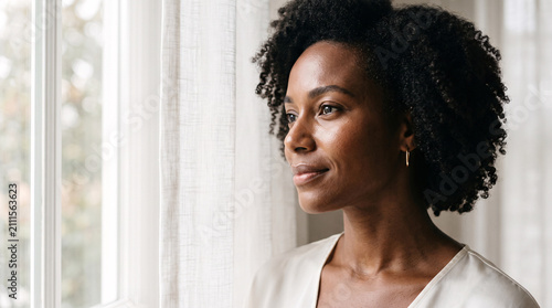 Thoughtful African American woman looking out of a bright window at home.