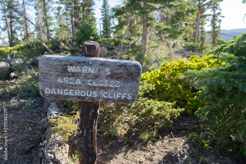 Fotografie Rustic, hand-painted wooden trail sign reading WARNING AREA CLOSED DANGEROUS CLIFFS stands on a wooden post in a forested outdoor setting, offset with background visible on the right side of frame