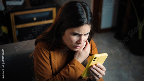 Принти на полотні Young Hispanic woman sitting on her sofa straining her eyes while using her smar