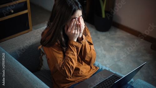 Fotografie Young Latina woman sitting on her sofa covering her face due to severe digital e