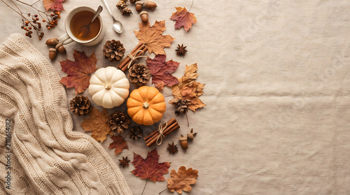 Autumn cozy flat lay with pumpkins, knitted sweater, dry leaves, cup of tea, and copy space on linen background