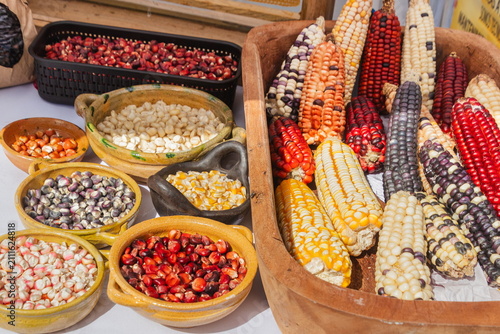Traditional colorful Indian corn cobs and multicolored dried corn kernels arranged on rustic wooden and clay bowls. An Ecuadorian farmers' market.
