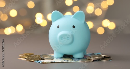 Woman putting coins into piggy bank against grey background with blurred lights, closeup. Bokeh effect