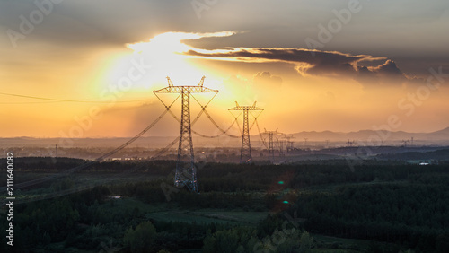 Foto High-voltage power transmission towers stand silhouetted against a sunset sky over a hilly, vegetated landscape
