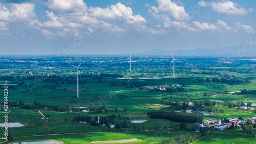 Obraz na płótnie Wind turbines are set in a sprawling green rural landscape with fields, ponds and scattered settlements under a cloudy blue sky