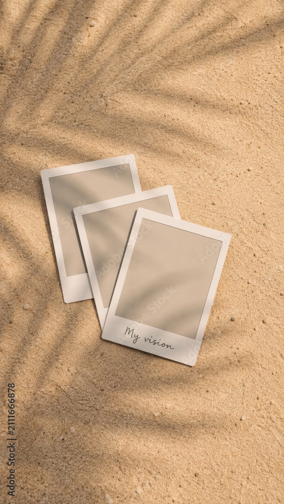 Fototapeta premium Blank instant photo prints on sandy background with palm leaf shadows.