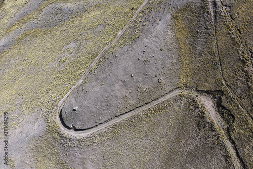 Bild auf Leinwand Winding gravel road switchbacking across an arid mountain hillside, aerial drone
