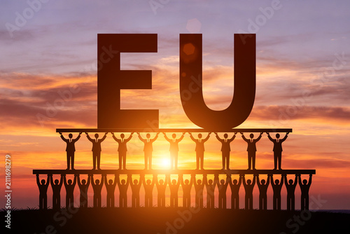 Tableau sur toile Numerous small figures silhouetted in the morning sun, holding up EU