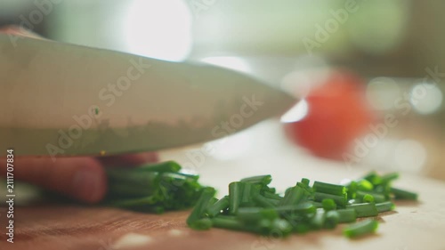 Woman’s hand chopping green onion with kitchen knife on wooden cutting board