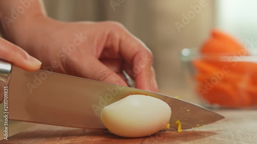 Close-up of woman hands cleanly slicing a boiled egg on a wood cutting board.
