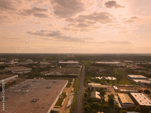 Aerial drone view of a massive logistics warehouse park and railroad tracks under a warm hazy sunset sky