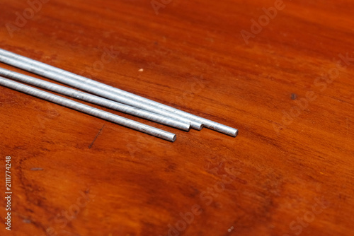 Fotografie few thin silver metal rods lying diagonally on a smooth wooden table surface