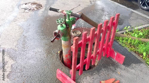 Fire hydrant with red fence and water pooling around it in urban street setting