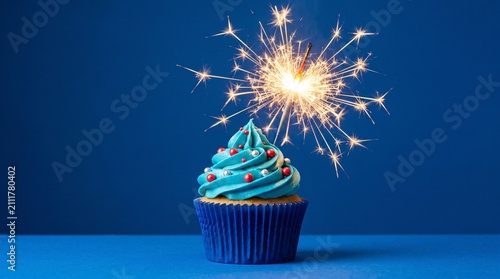Blue cupcake topped with glowing sparkler against solid vibrant background for festive celebration joyful occasion with frosting metallic sprinkles