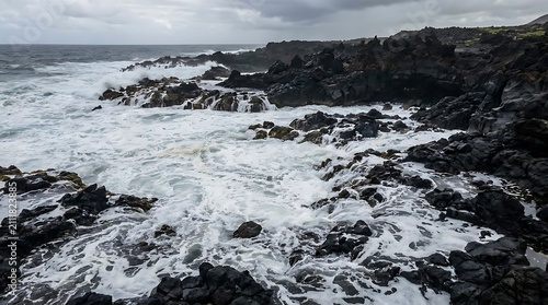 Ocean waves crash against dark volcanic rock coastline under cloudy sky