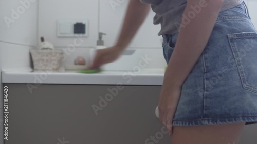 Woman wiping a bathroom countertop to remove dust, dirt and toothpaste marks during home cleaning