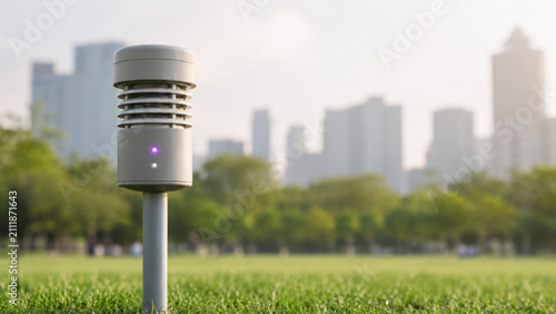 White air quality sensor on metal pole standing in green urban park lawn with blurred city skyline background and soft hazy light environmental monitoring technology