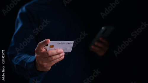 Konstfotografi Detailed view male hand holding plastic credit card, other hand holding mobile phone, performing secure online financial payment transaction inside dark studio background, representing e-commerce