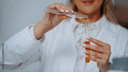 Canvastavla Female Scientist Pouring Amber Liquid Between Test Tubes in Laboratory Cosmetic