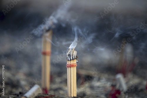 Fine smoke rises between the upright incense sticks and forms soft, swirling lines in the warm air. The bundles are carefully tied and depict a serene scene of traditional offerings such as those found in many temples and shrines, Wat Yai Chai Mongkon, Ayutthaya, Thailand