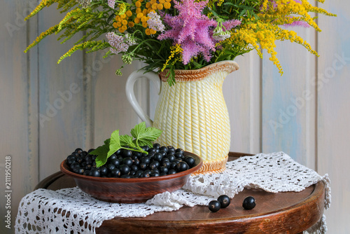 Rustic still life with a wildflower bouquet, fresh black currants and cozy countryside atmosphere