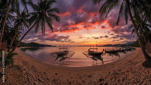 Tropical beach with boats at sunset under palm trees