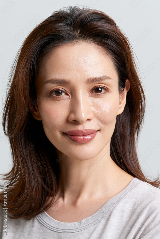Fototapeta premium japanese beauty model with luminous natural skin, elegant asian woman with brown hair and glossy gradient lips, mature cosmetic portrait with dewy skin and minimal makeup