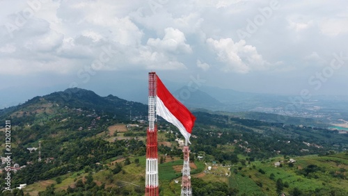 Quadro su tela Aerial drone view of the Indonesian national flag waving proudly atop a telecommunications tower overlooking a lush mountain landscape