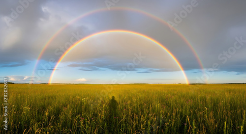 Double rainbow arching over lush green meadow with scattered wildflowers, stormy sky clearing, beautiful weather phenomenon, nature's beauty, vibrant colors.