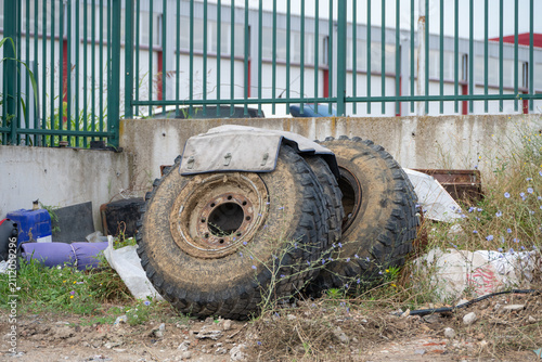 Bild auf Leinwand two large, muddy heavy-duty tires with rusty metal rims and an attached mudguard are abandoned on a dirt patch overgrown with weeds