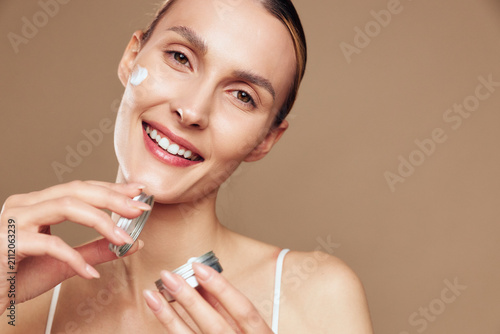 Obraz na płótnie Smiling woman applying face cream with hands in close up, skincare and self care concept, warm studio lighting on brown background, soft focus
