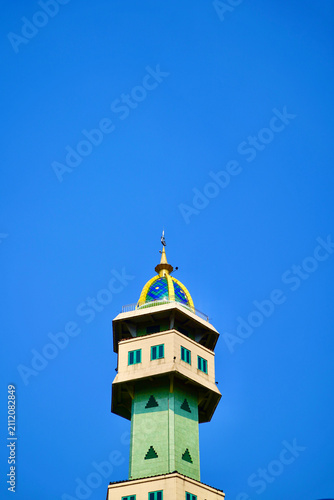Obraz na plátně Mosque Minaret with Dome
Low-angle view of a modern mosque minaret tower featuring a golden dome and green windows against a vibrant clear blue sky background for religious design