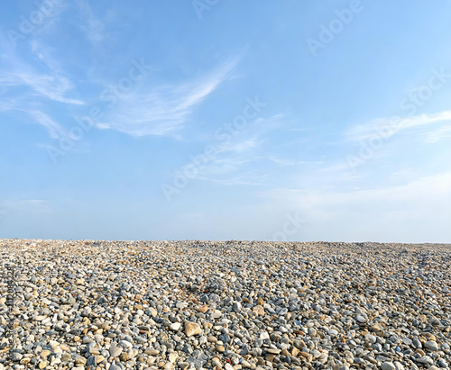 A vast expanse of smooth pebbles stretches to the horizon beneath a clear blue sky with wispy clouds.