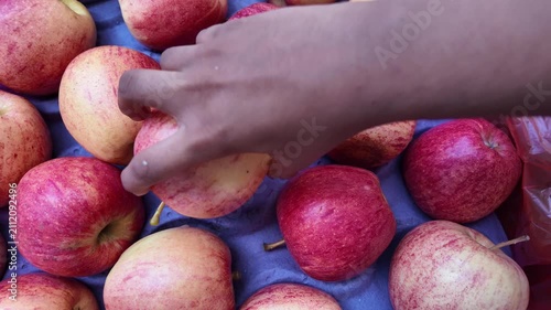 Red apples are in boxes at supermarket. Girl takes red apple, examines it  , fresh apples