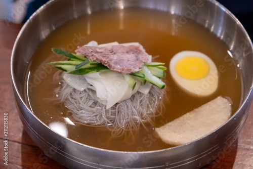 Korean cold buckwheat noodles or Naengmyeon served in a chilled beef broth, topped with sliced beef, cucumber, pickled radish, half a boiled egg, and tofu.