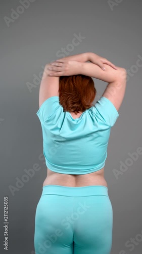 Unrecognizable curvy woman performs exercises for muscles of upper back, arms and shoulder joint, posture correction and physical therapy concept on gray background