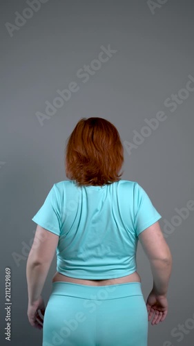 Unrecognizable curvy woman performs exercises for muscles of upper back and shoulder joint, posture correction and physical therapy concept on gray background
