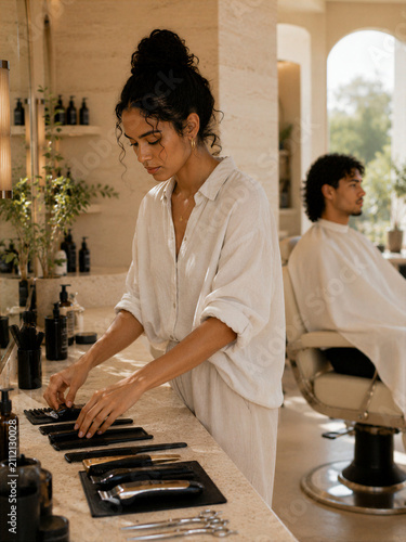 Woman organizing tools in a hair salon while a client sits in a chair