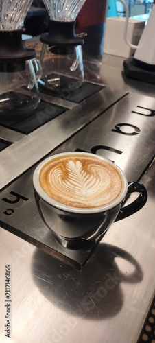 Foto Fresh latte with leaf latte art served on a café counter beside pour over coffee equipment, showcasing specialty coffee, barista craftsmanship, and modern coffee culture