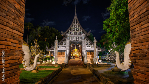 Foto Ancient Lanna style teak wooden viharn of Wat Lok Moli illuminated at night, framed by brick archways in Chiang Mai, Thailand